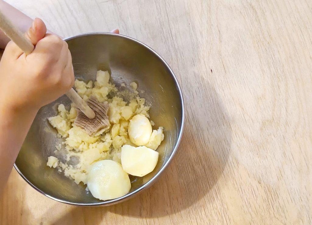 Kind stampft Kartoffeln